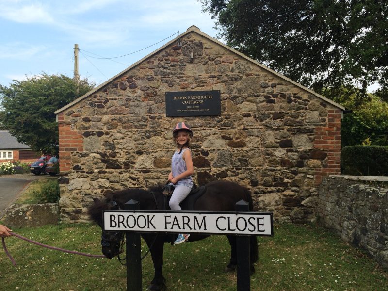 Young girl on pony behind brook farm close sign